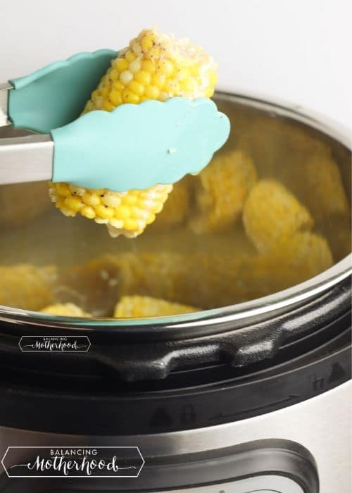 teal tongs removing corn on the cob from instant pot