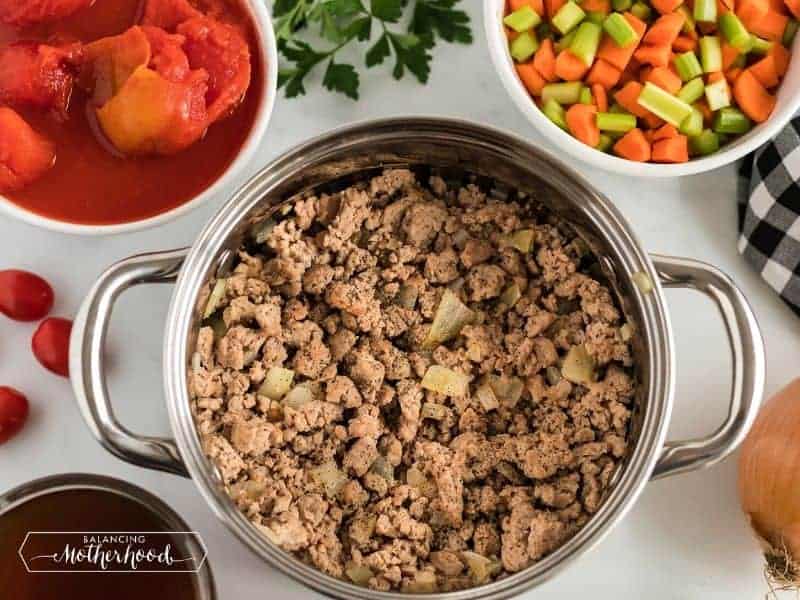 ground beef in pot, with sides of celery and carrots, an onion, and tomatoes