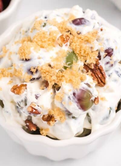 Grape salad recipe in a white bowl, topped with pecans and brown sugar.