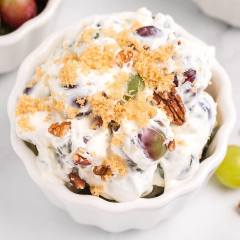 Grape salad recipe in a white bowl, topped with pecans and brown sugar.