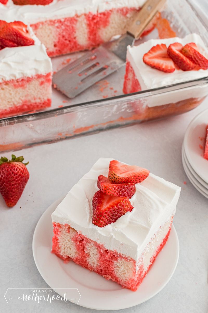 piece of strawberry poke cake on plate, with casserole dish in background