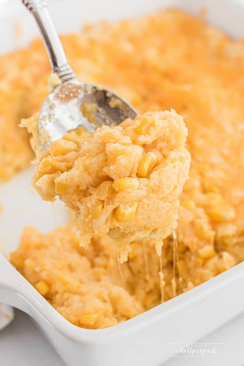 spoonful of corn casserole with cheese dripping from spoon