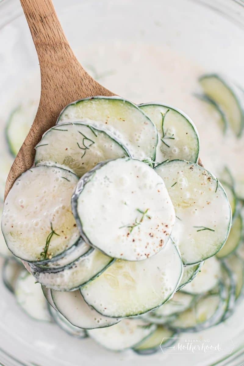 wooden spoon lifting cucumber salad serving from bowl