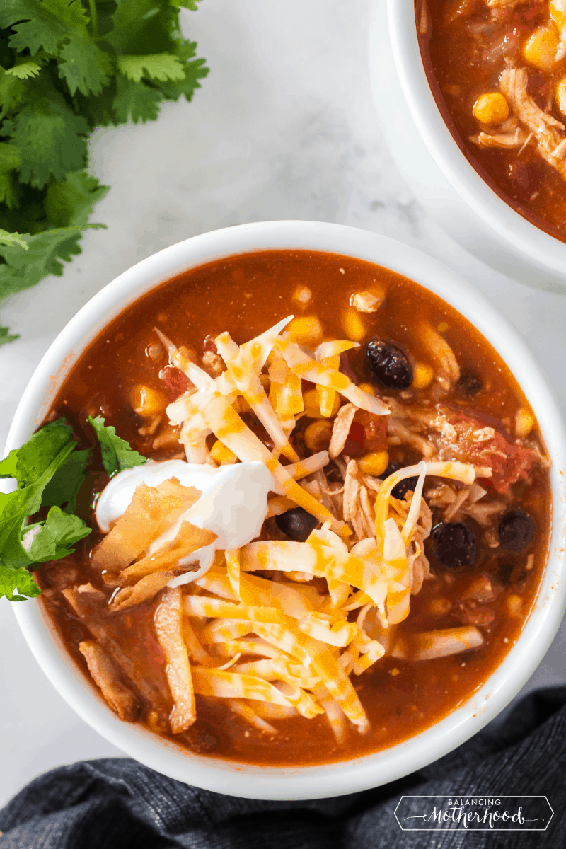Bowl with chicken tortilla soup, topped with cheese, tortilla strips, and sour cream.