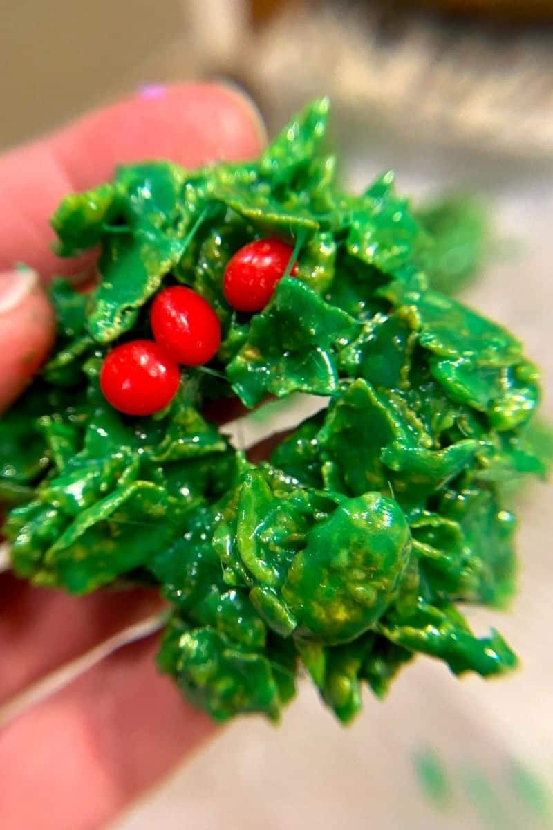 hand holding up a bright green wreath cookie with three red hots