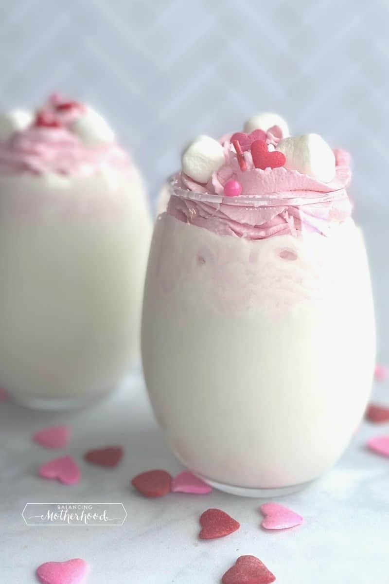 clear glass with milk and whipped strawberry cream on top with marshmallows and heart sprinkles