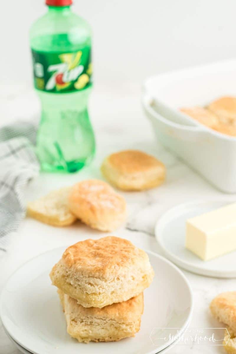 two biscuits stacked on plate with butter, and 7UP in the background