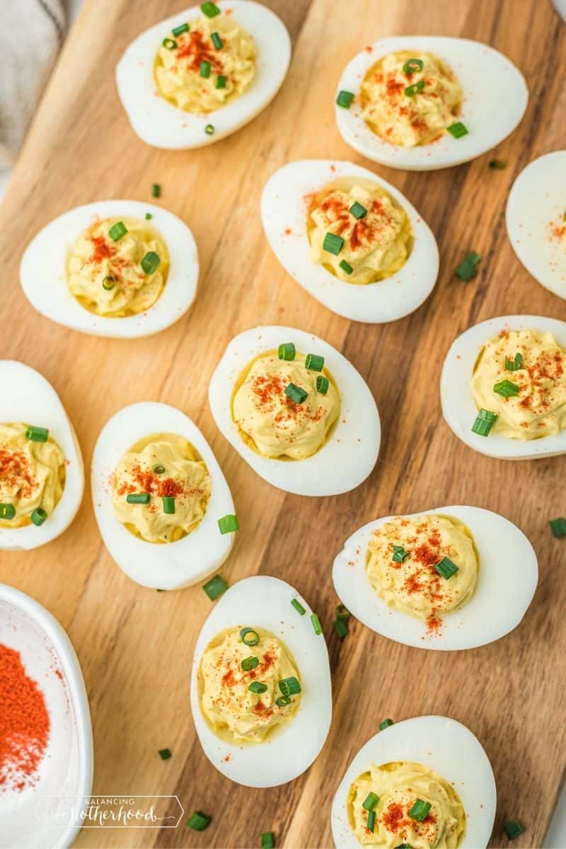 wooden cutting board with deviled eggs topped with paprika and green onions