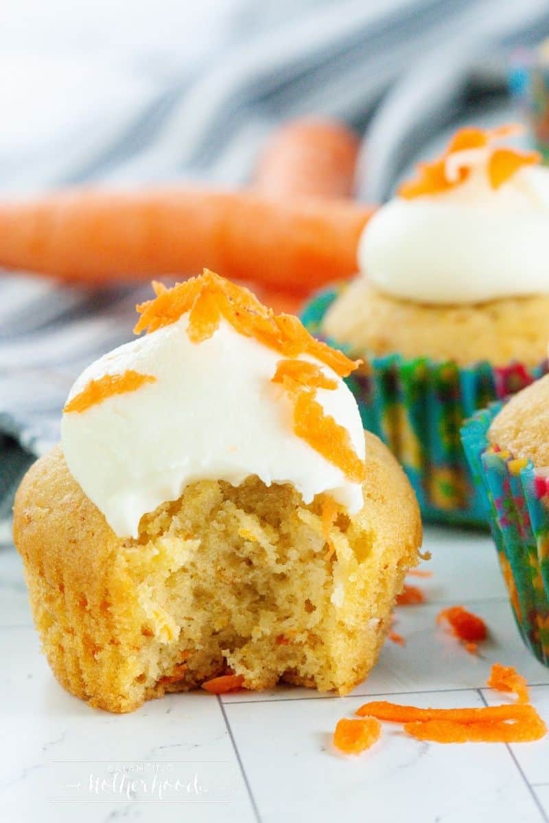 cupcake with bite out topped with dollop of cream cheese frosting and carrot garnish