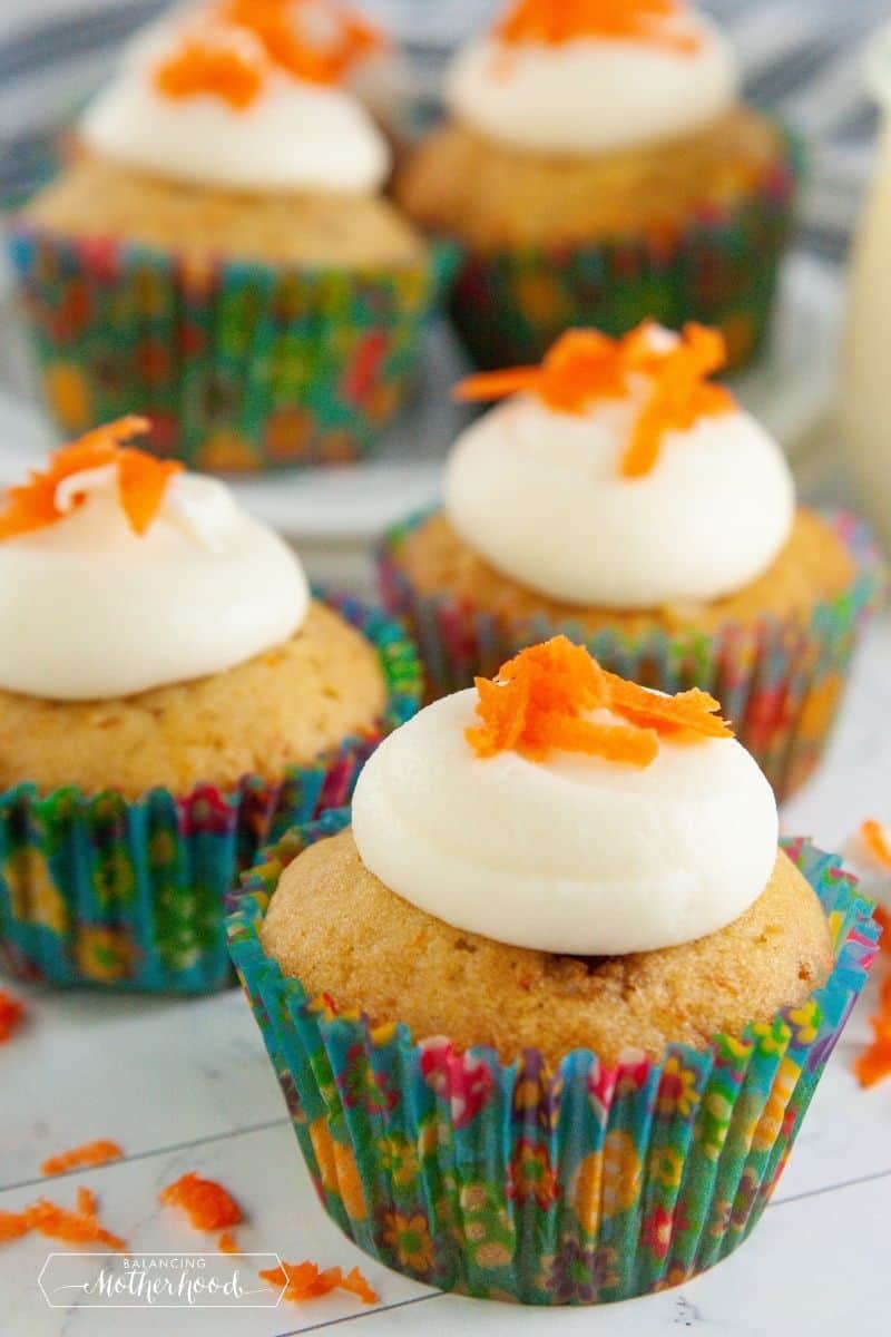 carrot cake cupcakes with a dollop of cream cheese frosting on top with shaved carrots for garnish
