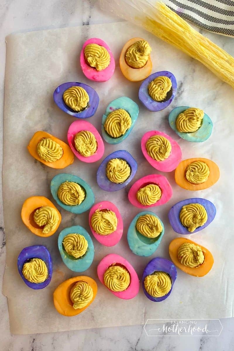 pink, orange, blue, and purple egg whites with deviled egg mixture pipped in middle
