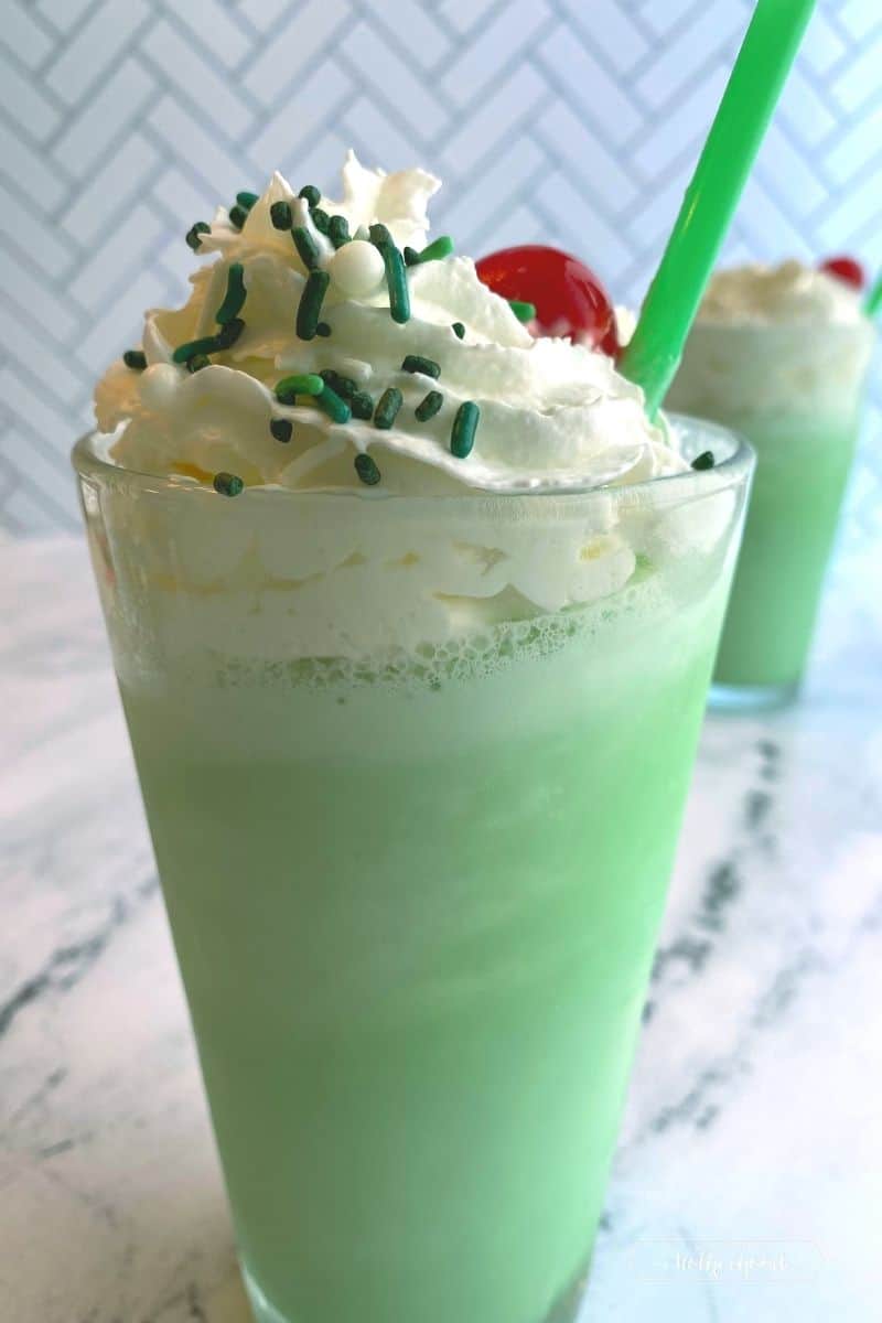 green milkshake with whipped cream and a cherry with green and white sprinkles and a green straw