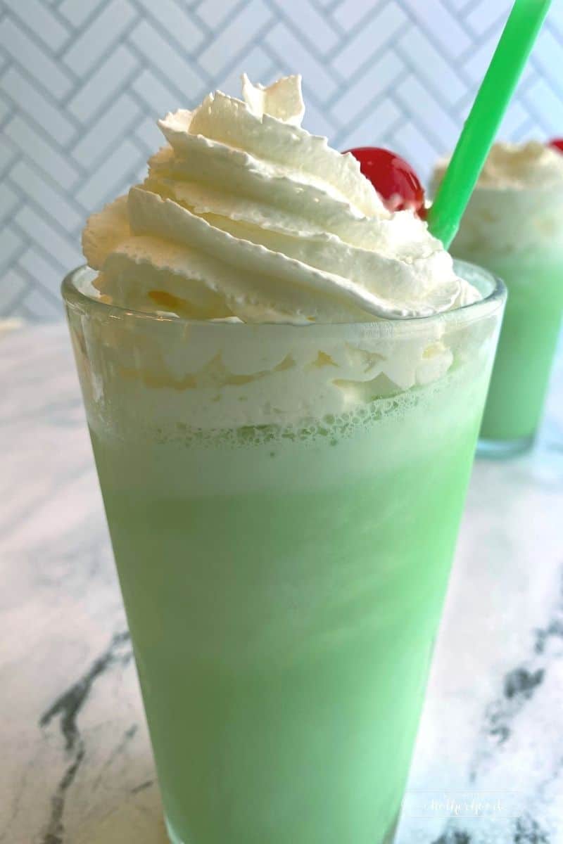glass with green shake topped with whipped cream and a cherry with a green straw