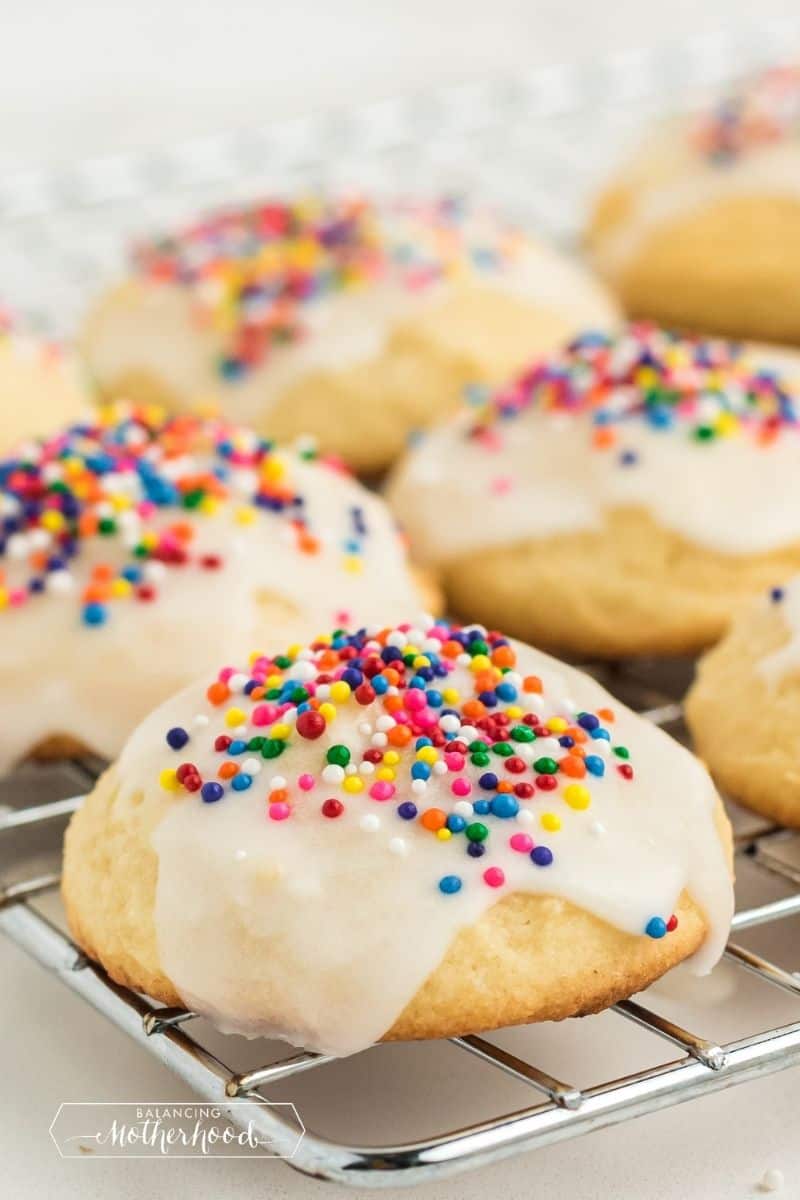 close up of italian ricotta cookie with rainbow sprinkles and frosting dripping down the side of the cookie