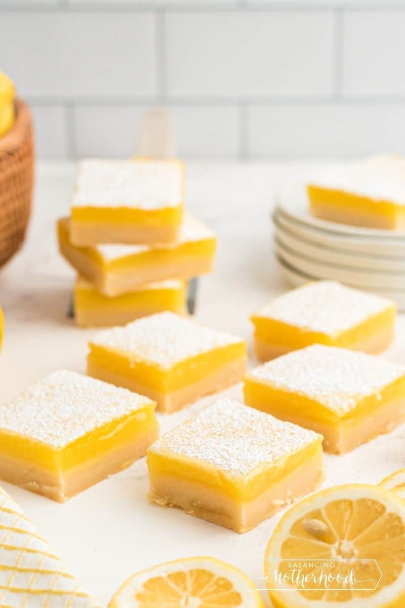 five lemon bars on table with lemon cut in half, three stacked in background
