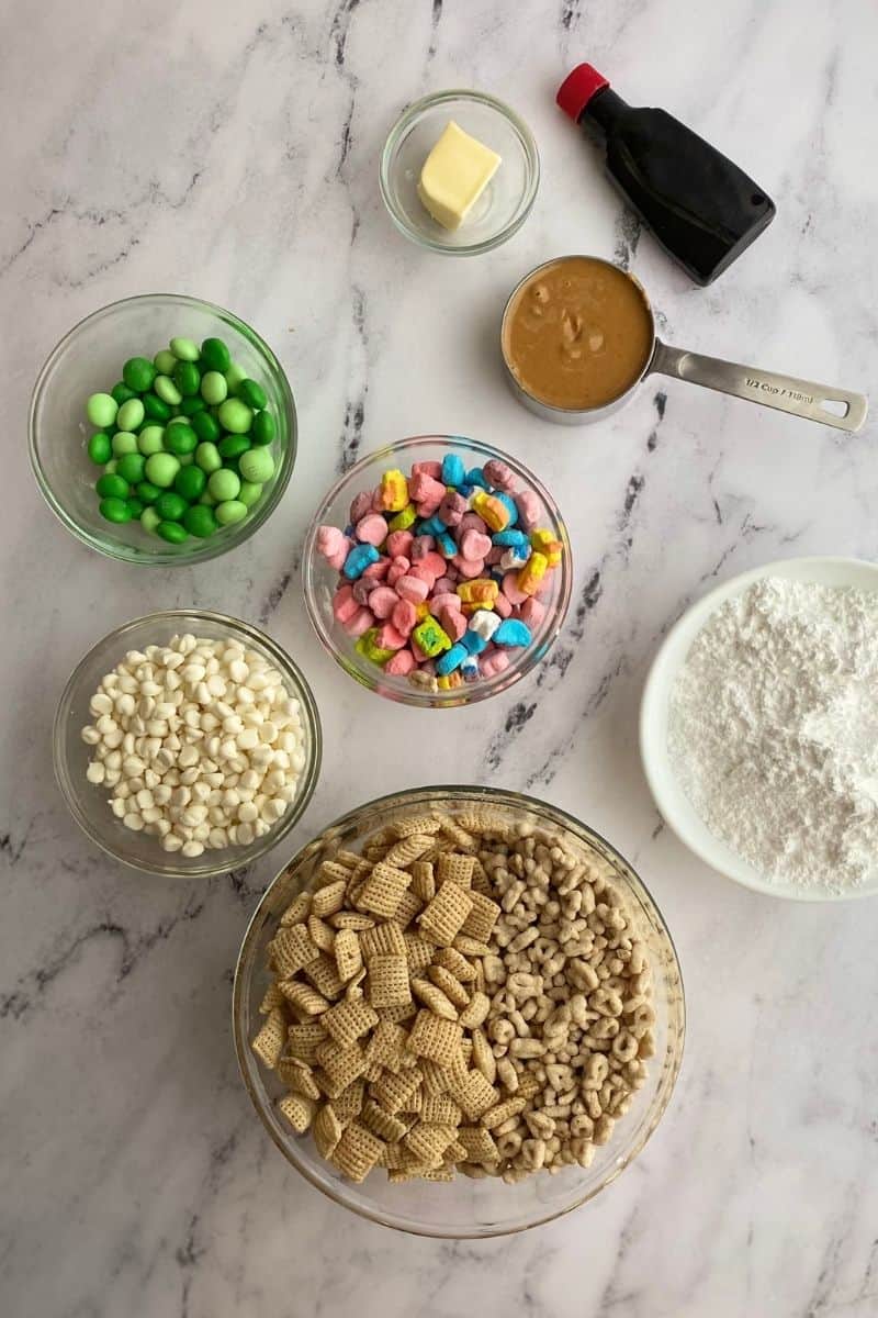lucky charms muddy buddy ingredients: green M&Ms, white chocolate chips, Chex cereal, lucky charms cereal, lucky charms marshmallows, peanut butter, butter, vanilla