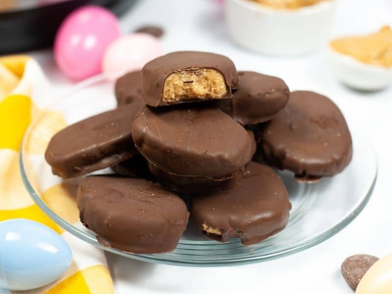 stack of peanut butter eggs on clear plate with easter eggs in background