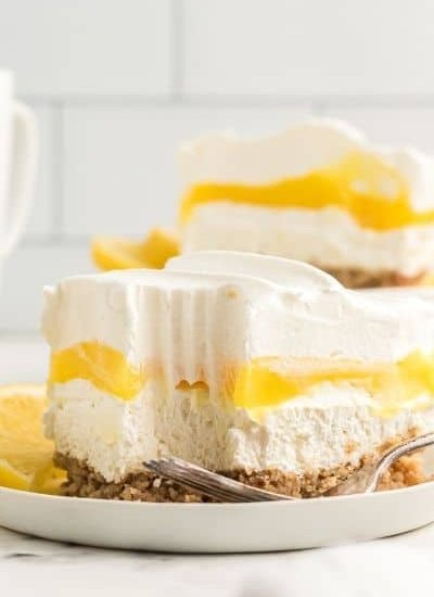 slice of lemon lush where you can see the pecan crust topped with a white layer, then a bright yellow layer all topped with whipped cream