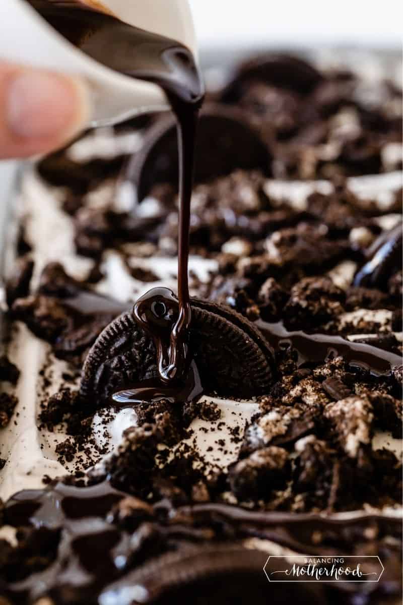 chocolate sauce being drizzled over an oreo cookie on top of the cake
