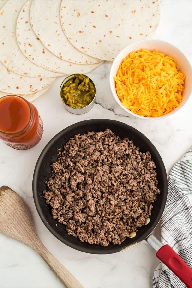 ingredients: ground beef, cheese, chiles, enchilada sauce, with tortillas spread out on counter