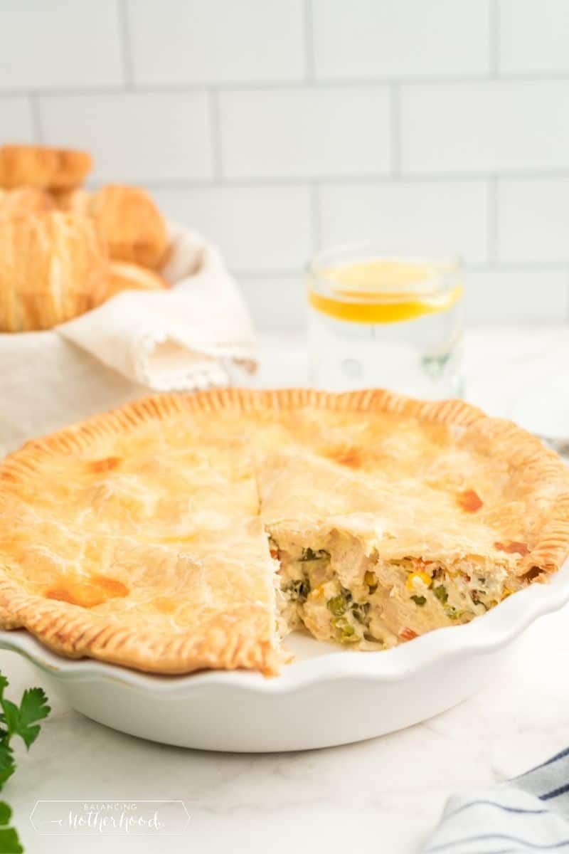 pot pie in white pie dish with slice removed. You can see chicken and green vegetables inside