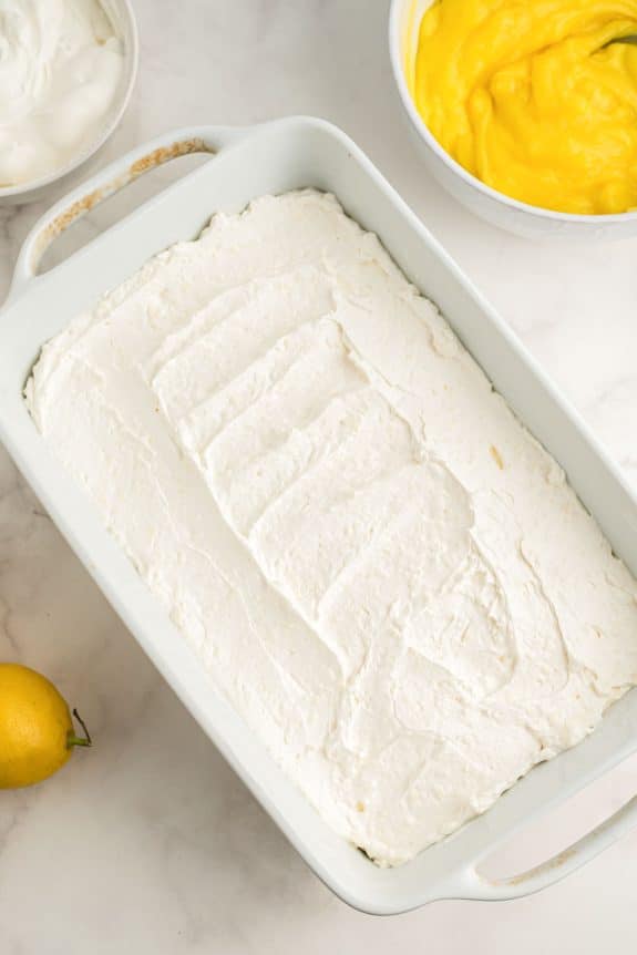 A Lemon Lush dessert displayed in a white baking dish, topped with swirls of whipped cream.