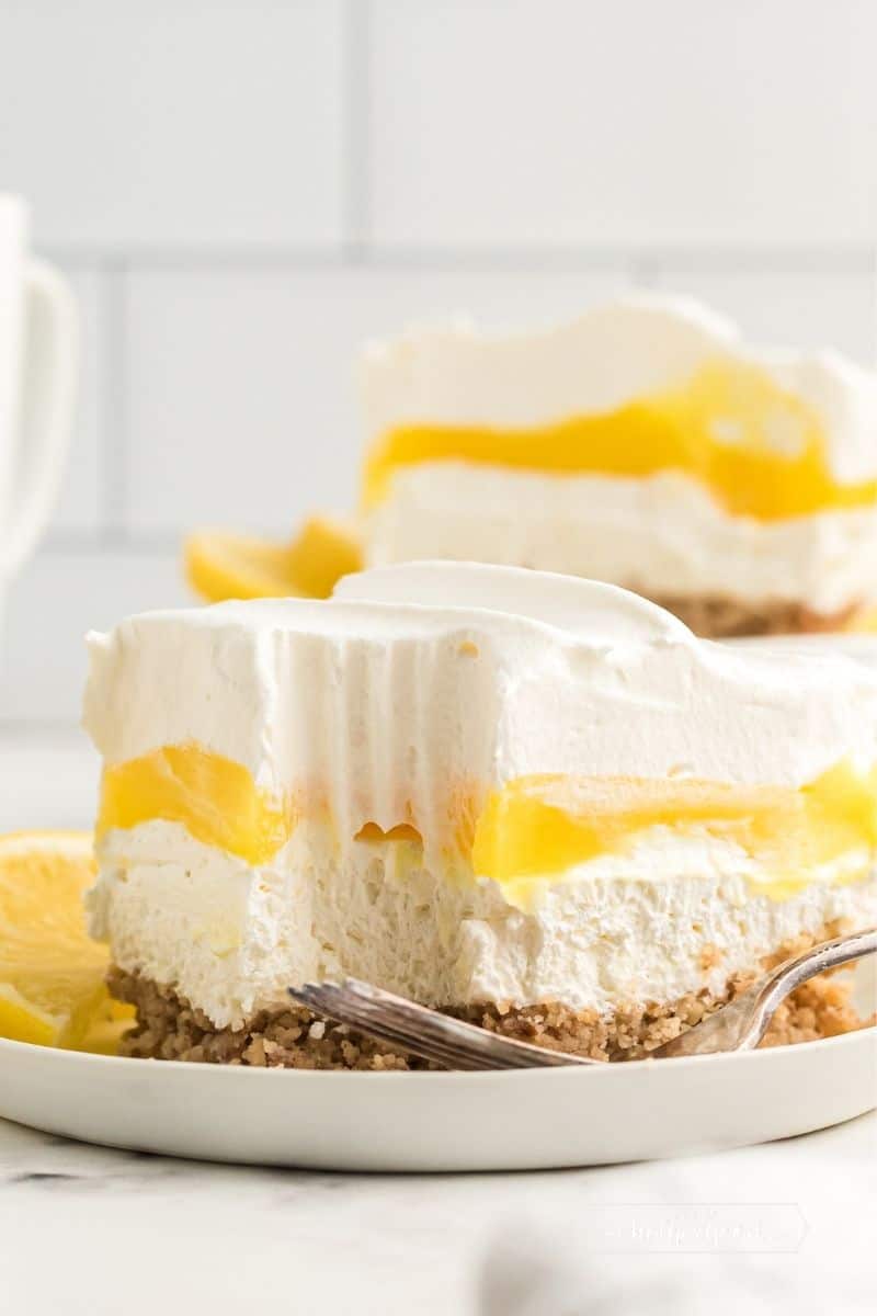 slice of lemon lush where you can see the pecan crust topped with a white layer, then a bright yellow layer all topped with whipped cream