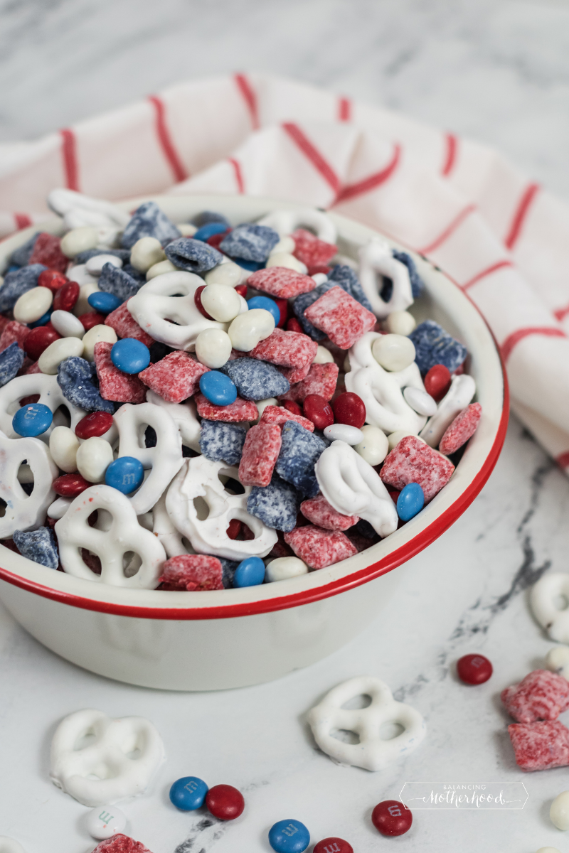 white pretzels with red and blue coated cereal and red, white, and blue M&Ms in white bowl with red and white tea towel on counter