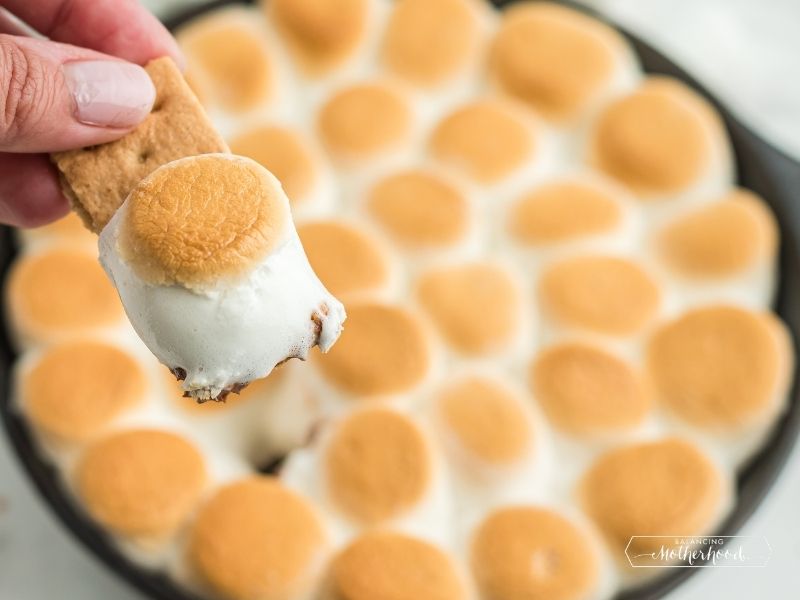 skillet with golden marshmallows and melted chocolate, with large golden marshmallow on graham cracker
