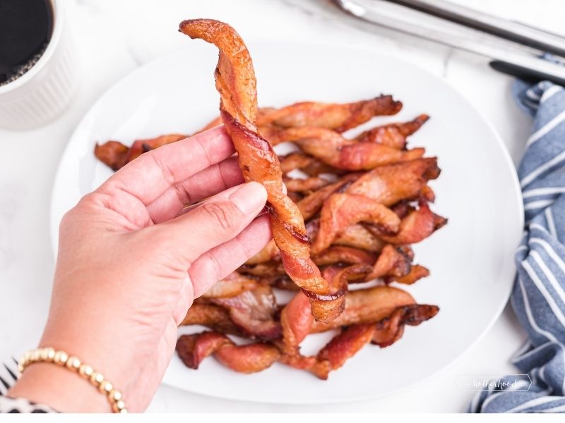 hand holding up a piece of twisted bacon