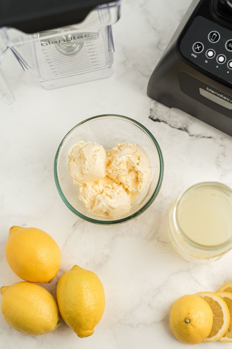 blender, vanilla ice cream in glass bowl, glass of lemonade and lemons on counter