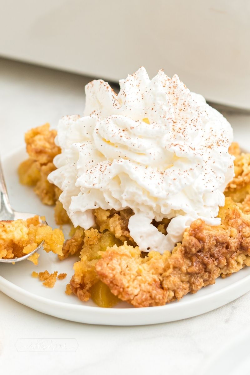peach dump cake on white plate with whipped cream and cinnamon