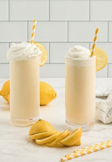 two glasses with yellow frosted lemonades with whipped cream and a yellow and white straws
