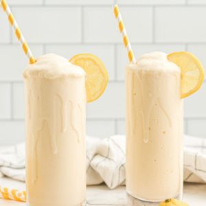 two glasses with yellow frosted lemonades with whipped cream and a yellow and white straws