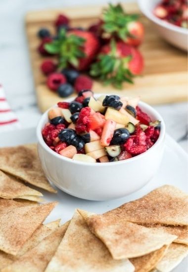 white bowl with fruit salsa and strawberries in background