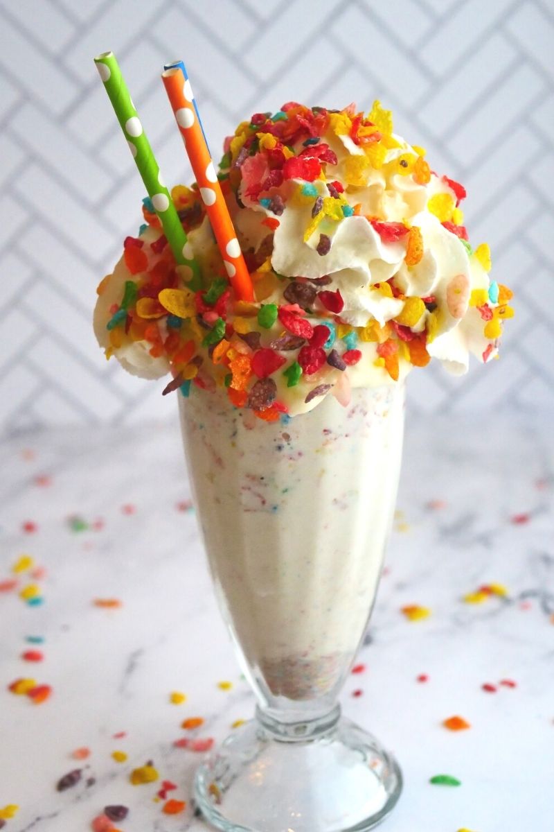 milkshake glass with whipped cream and fruity pebbles and three polka dot straws