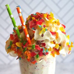tall milkshake glass with tons of whipped cream and fruity pebbles with three colored polka-dot straws