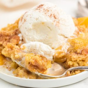 peach dump cake on white plate with spoon and topped with vanilla ice cream