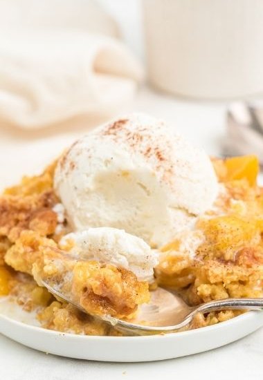 peach dump cake on white plate with spoon and topped with vanilla ice cream