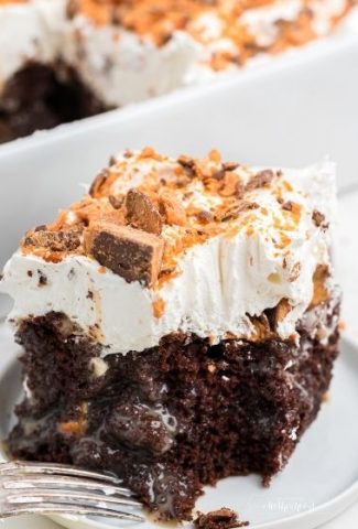 square piece of chocolate cake with whipped cream and butterfinger candy pieces on top with fork on the side