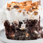 close up of chocolate butterfinger poke cake with thick layer of whipped cream and Butterfinger candies on top