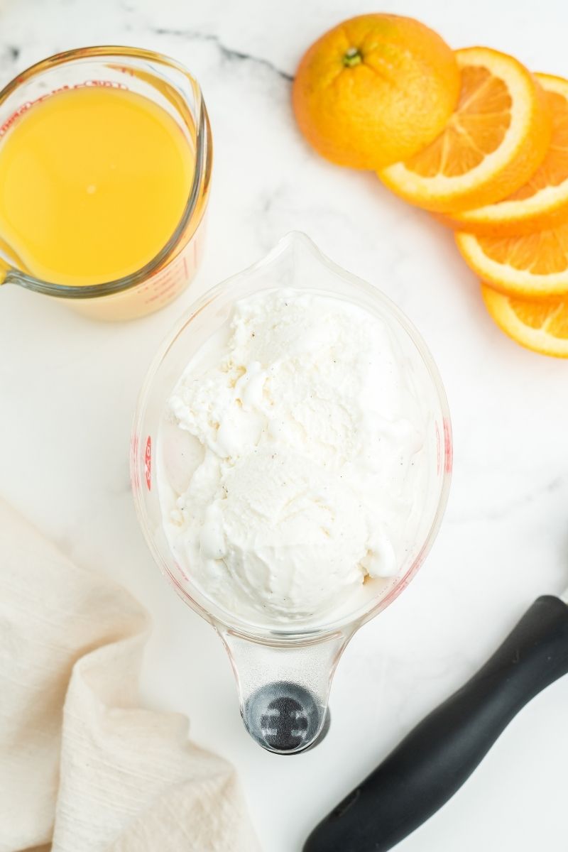 white counter with measuring glass with orange juice, sliced oranges, and large measuring cup with vanilla ice cream