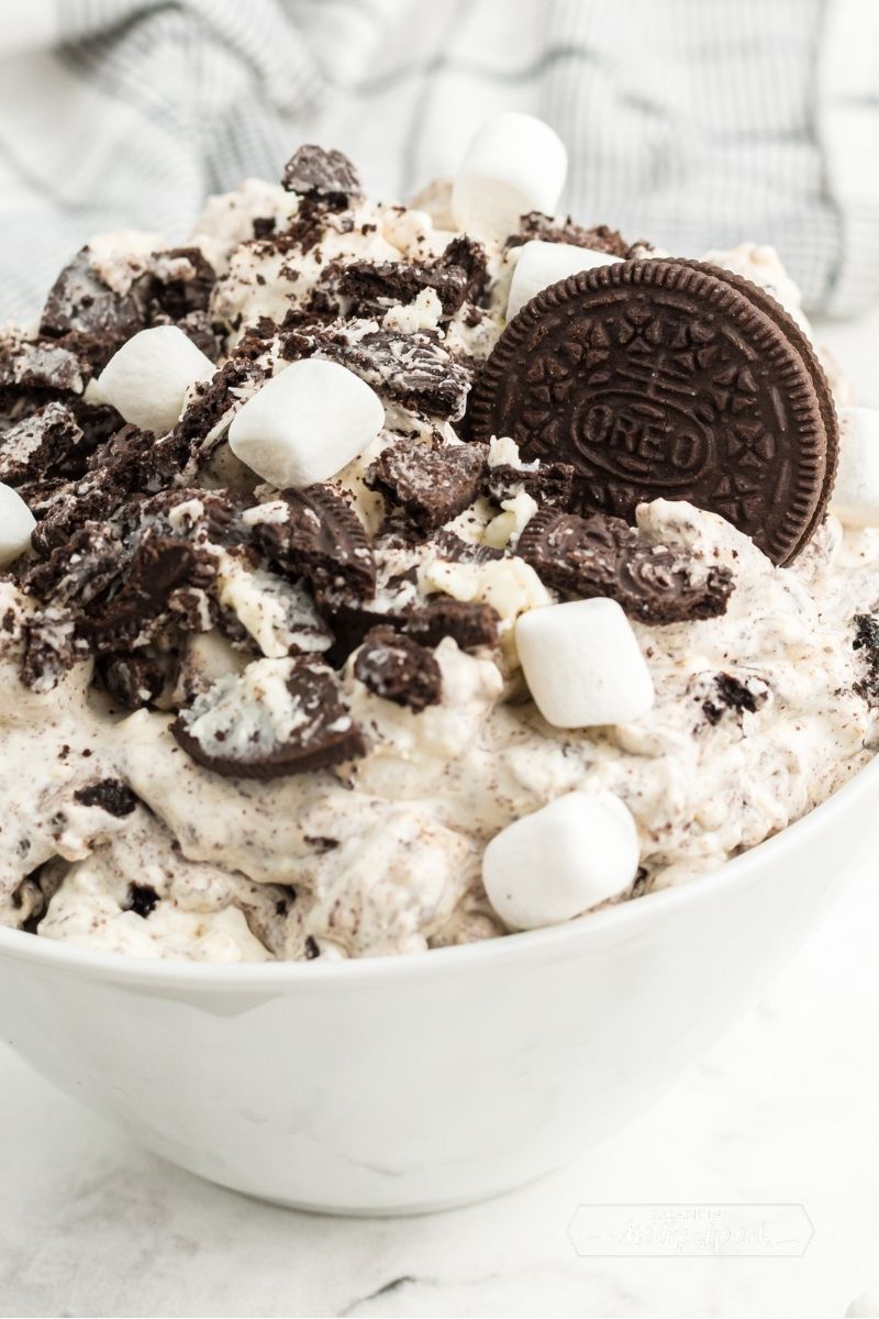 white bowl piled high with white Oreo fluff with one whole Oreo as garnish with mini marshmallows and crushed oreos on top.