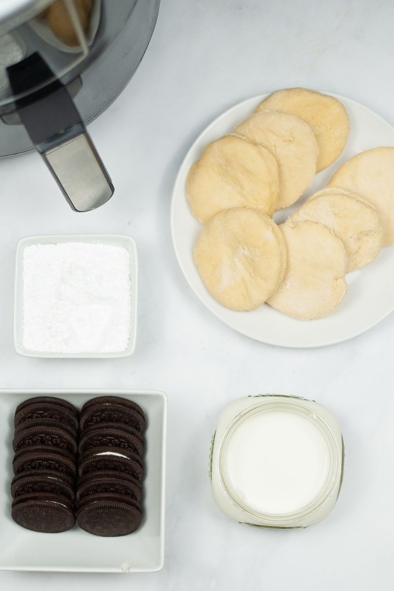 white counter with air fryer, biscuits, powdered sugar, Oreos, and milk