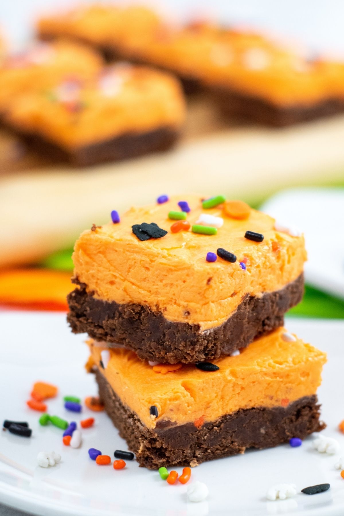 Two square chocolate cookies with thick orange buttercream and Halloween sprinkles.