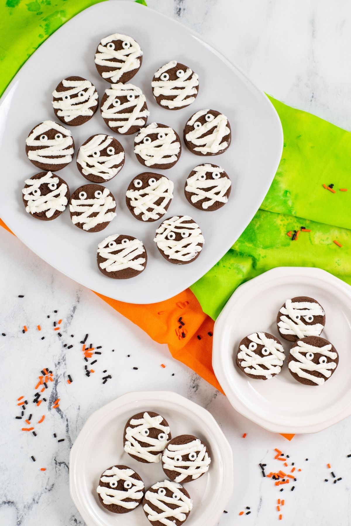 round chocolate cookies with mummy buttercream stripes and candy eyes on white plates