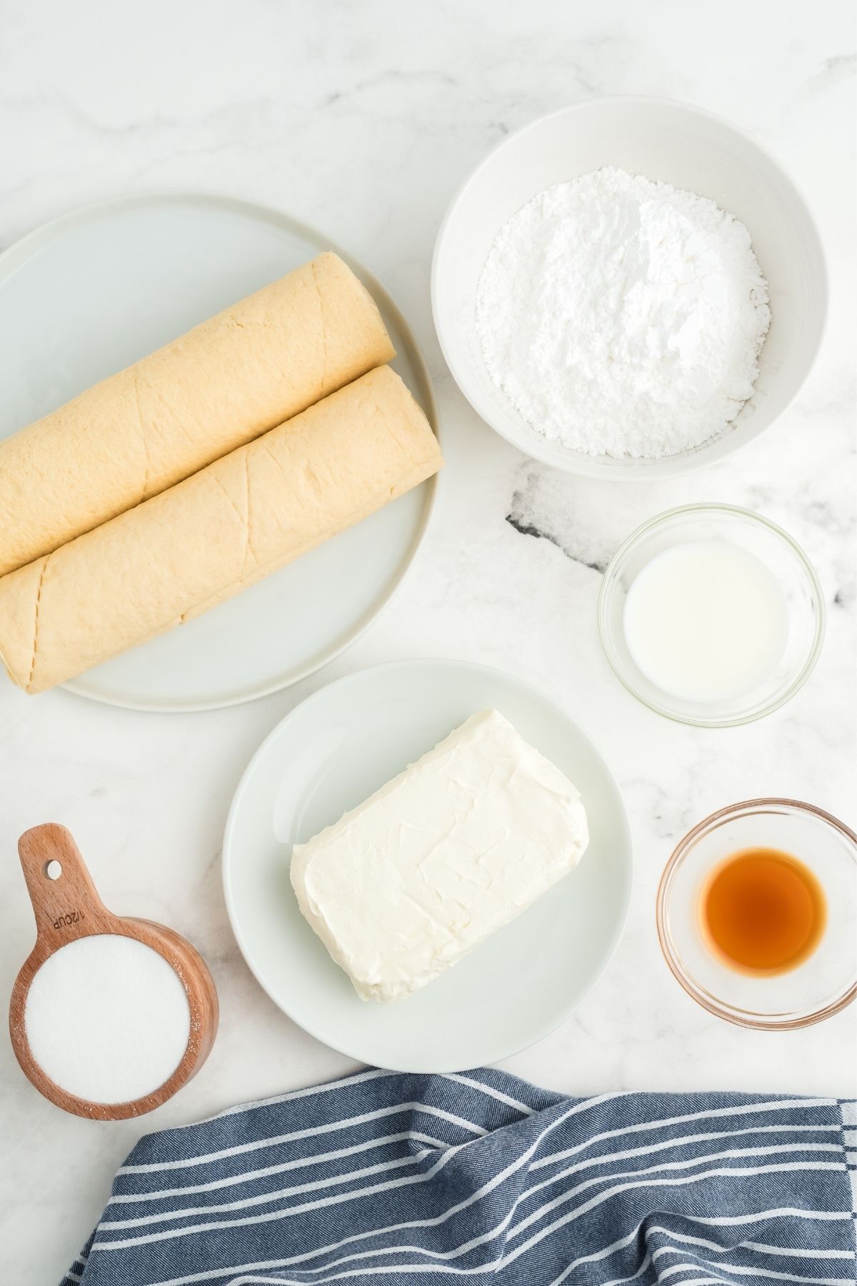 ingredients on white counter: 2 crescent rolls, powdered sugar, milk, vanilla, cream cheese, sugar