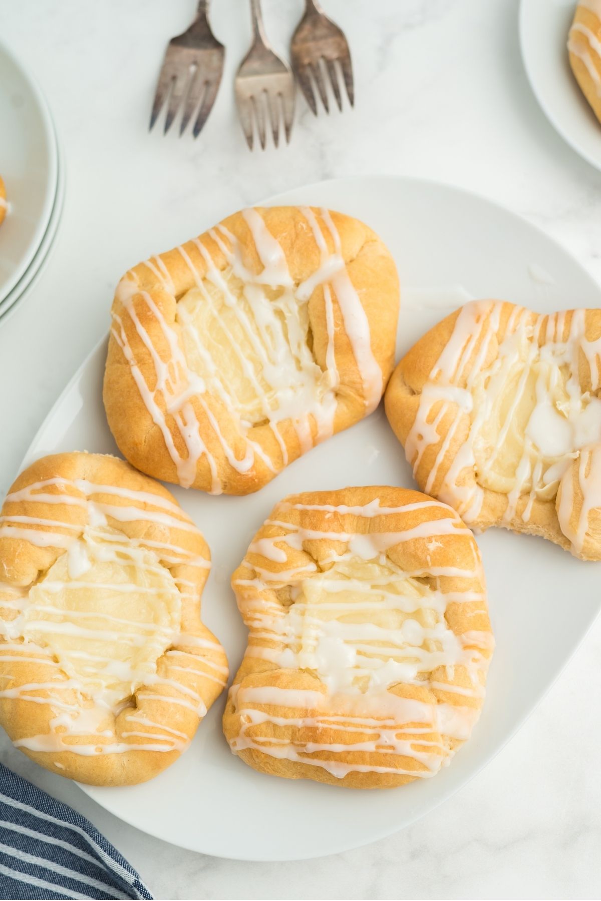 four cream cheese danishes with white glaze on white plate