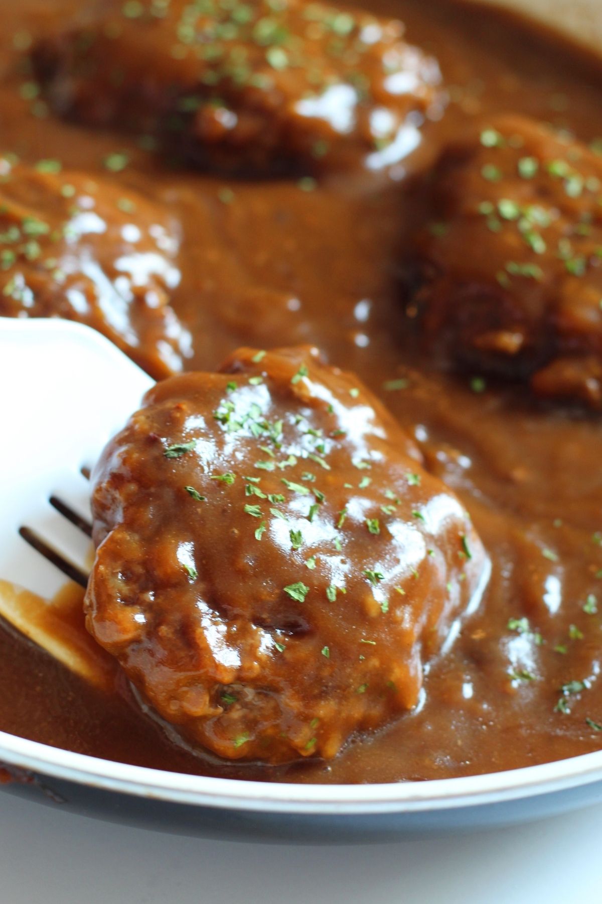 beef patties in sauce pan with brown gravy and parsley