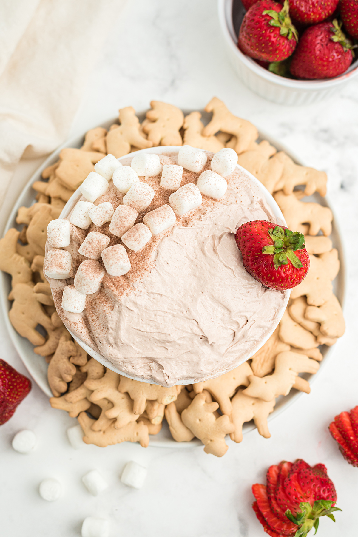Hot chocolate dip top view photo on a white counter with strawberries, crackers, and mini marshmallows.